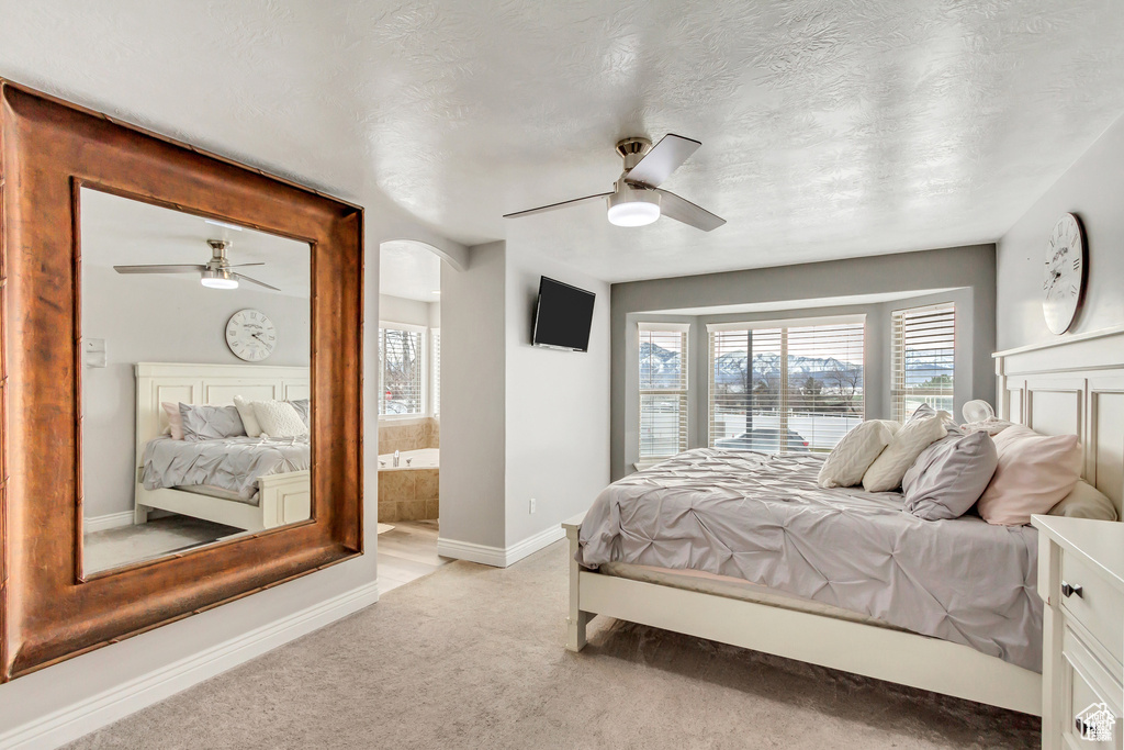 Bedroom featuring light carpet, baseboards, a ceiling fan, ensuite bathroom, and a textured ceiling