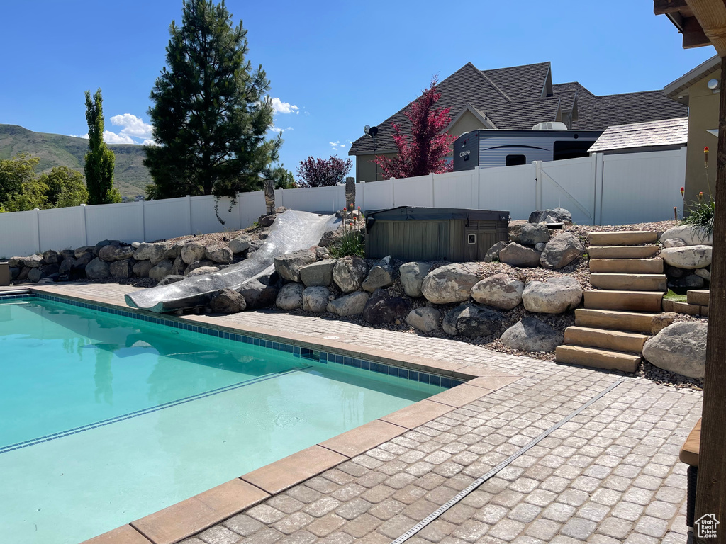 View of swimming pool with a hot tub, a fenced backyard, a patio, and a mountain view
