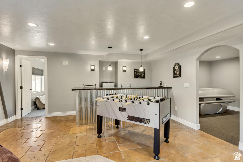 Recreation room with recessed lighting, stone tile flooring, baseboards, arched walkways, and a dry bar