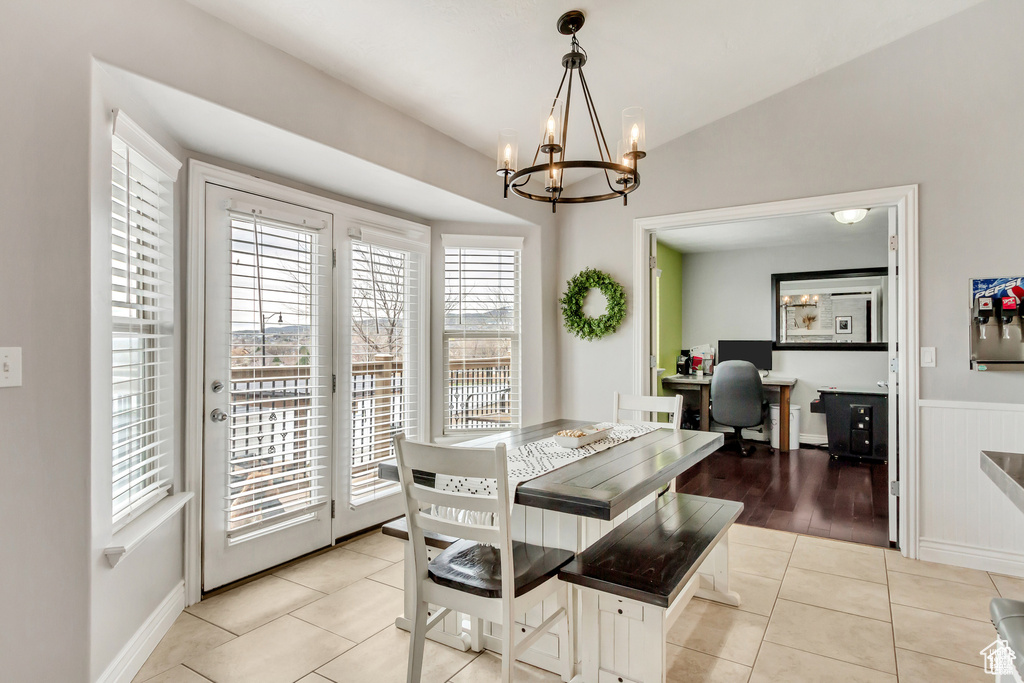 Dining area featuring a chandelier, plenty of natural light, light tile patterned flooring, a wainscoted wall, and vaulted ceiling