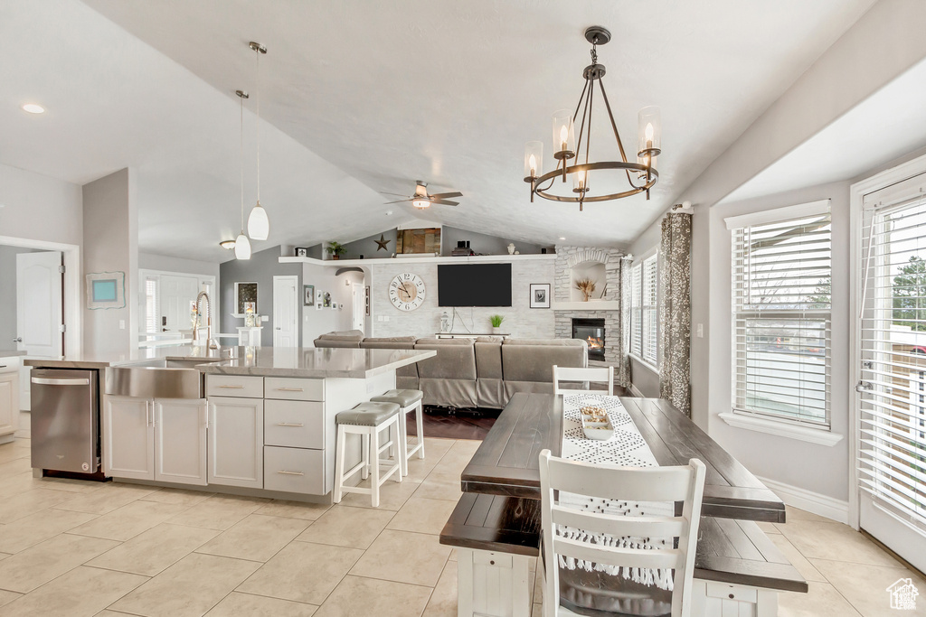 Dining room featuring ceiling fan, a chandelier, healthy amount of natural light, light tile patterned flooring, and vaulted ceiling