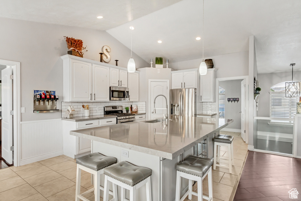 Kitchen with appliances with stainless steel finishes, a sink, white cabinets, decorative backsplash, and vaulted ceiling