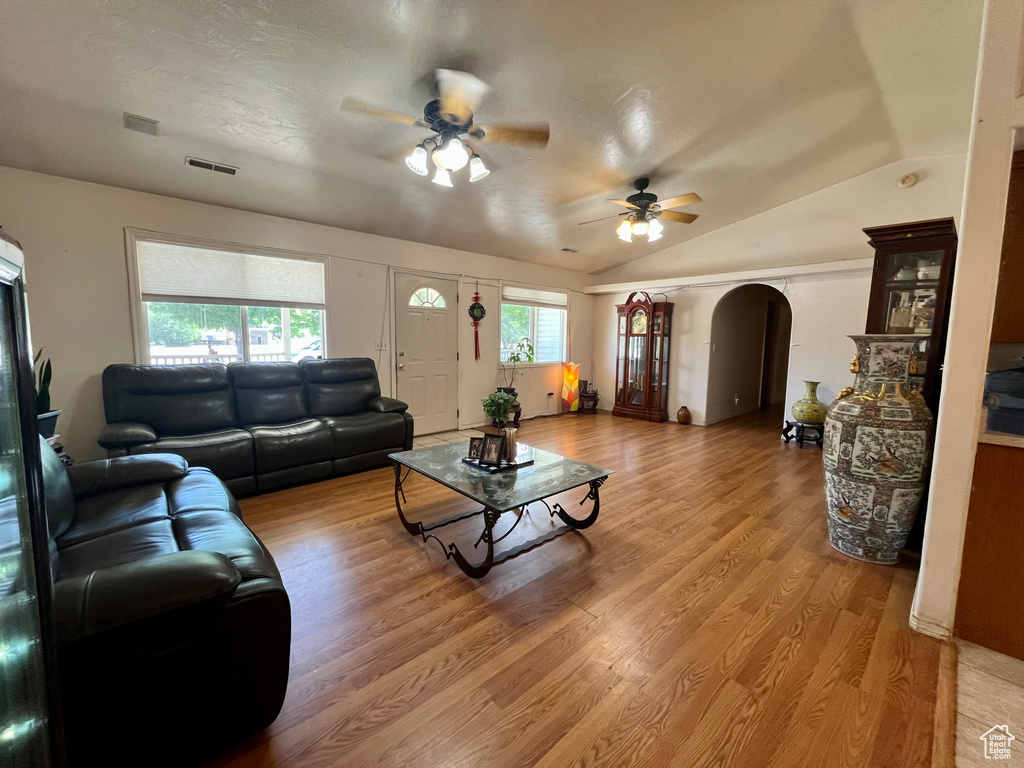 Living room with arched walkways, a ceiling fan, light wood-style flooring, and lofted ceiling