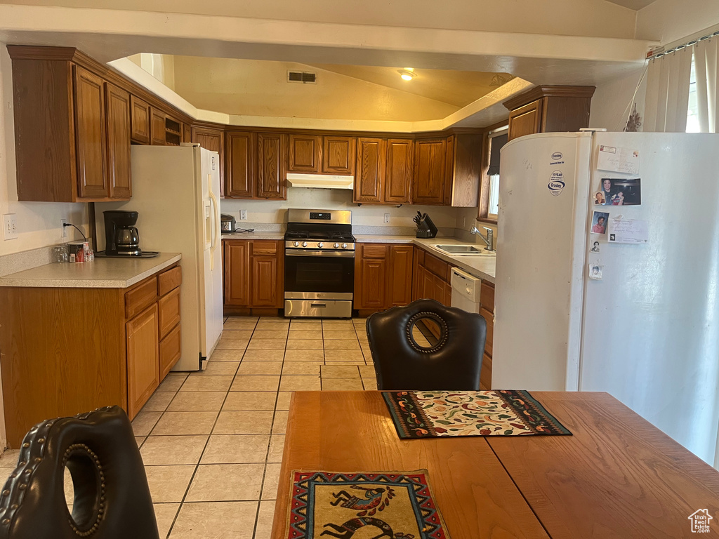 Kitchen featuring white appliances, under cabinet range hood, a sink, light tile patterned flooring, and light countertops