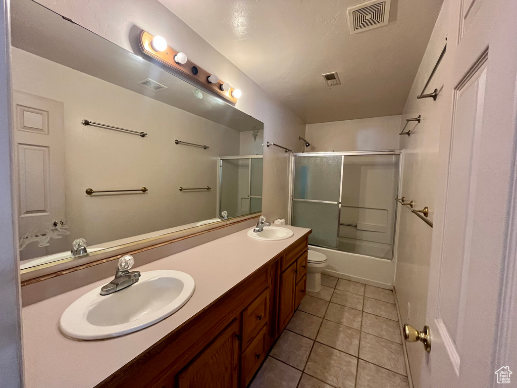 Full bathroom featuring double vanity, toilet, tile patterned flooring, and combined bath / shower with glass door