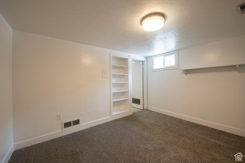 Basement with a textured ceiling, carpet, baseboards, and built in features
