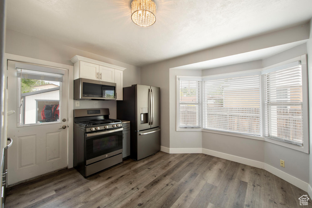 Kitchen featuring appliances with stainless steel finishes, baseboards, white cabinetry, wood finished floors, and a chandelier