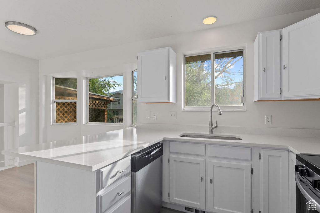 Kitchen with appliances with stainless steel finishes, a sink, a peninsula, white cabinets, and light countertops