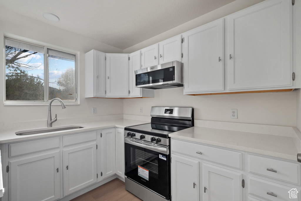 Kitchen featuring appliances with stainless steel finishes, a sink, white cabinetry, light countertops, and light wood-type flooring