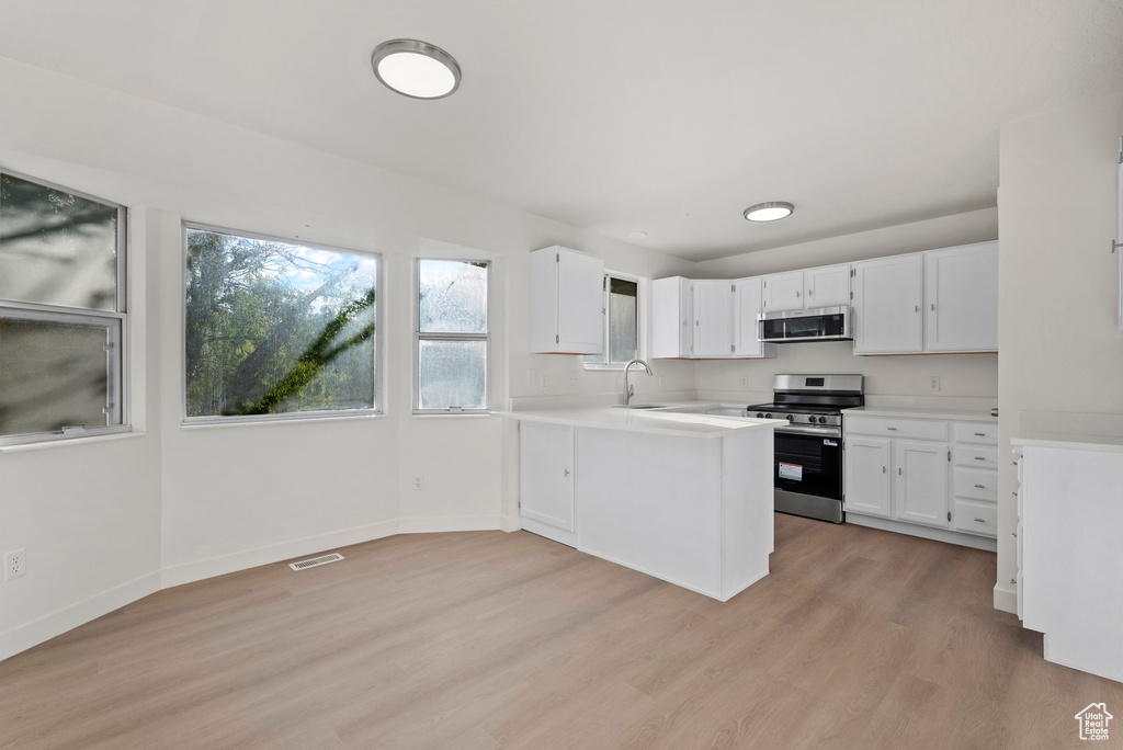Kitchen with appliances with stainless steel finishes, light countertops, white cabinetry, a sink, and light wood-style flooring