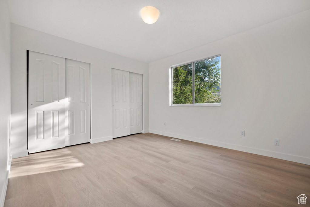 Unfurnished bedroom with two closets, baseboards, and light wood finished floors