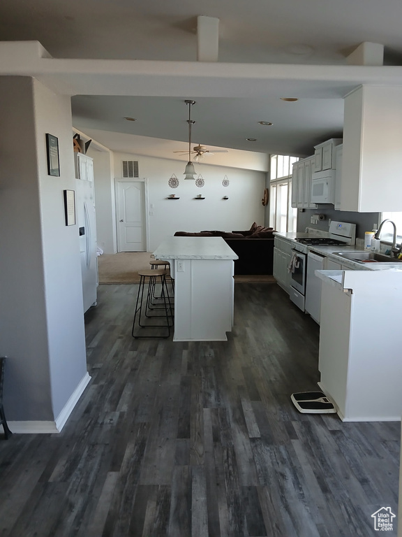 Kitchen with white appliances, a kitchen island, dark wood finished floors, white cabinetry, and decorative light fixtures