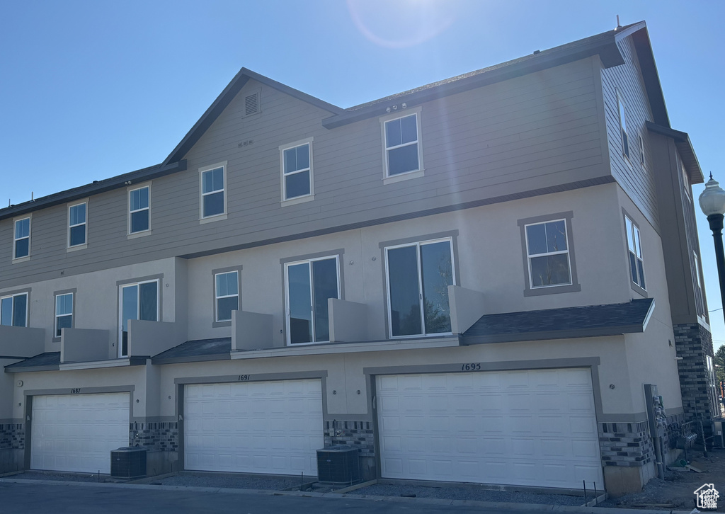 View of front of property featuring stone siding, an attached garage, stucco siding, and central air condition unit