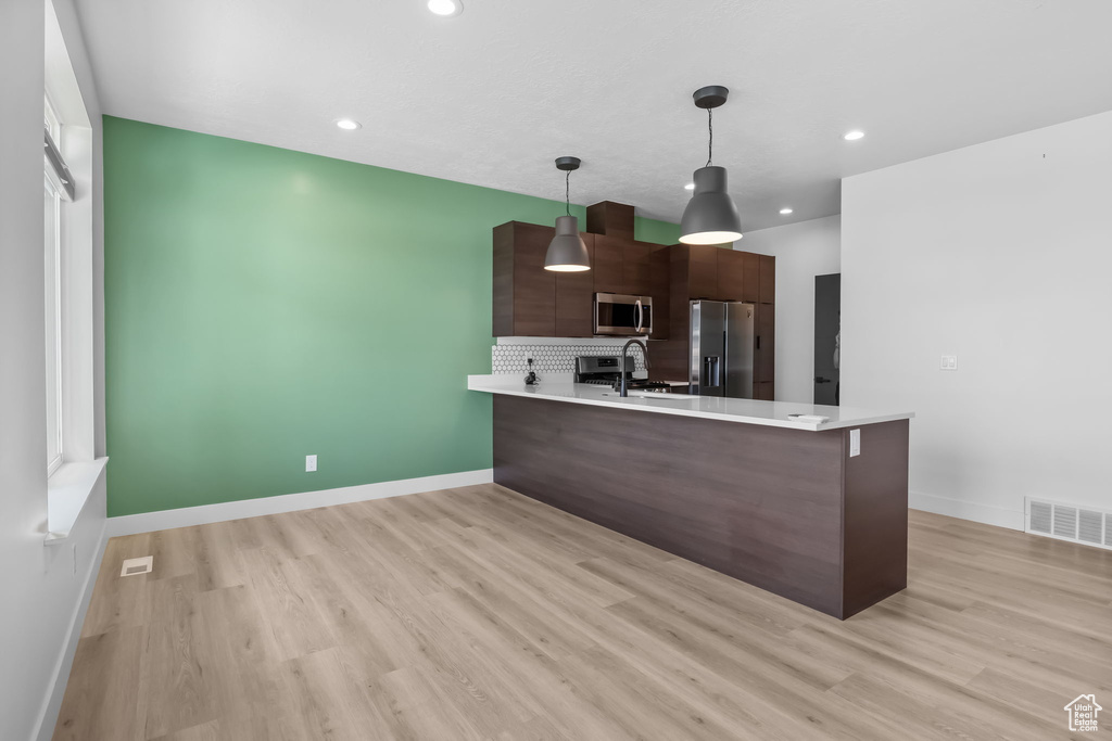 Kitchen featuring stainless steel appliances, light countertops, a peninsula, light wood-style flooring, and recessed lighting