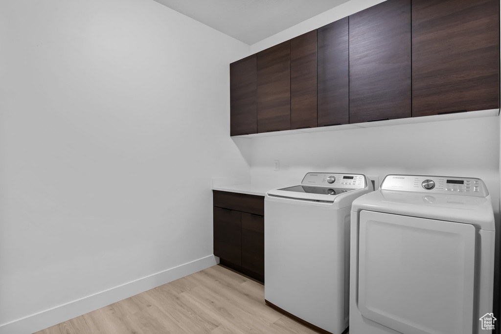 Laundry area with cabinet space, washing machine and clothes dryer, light wood finished floors, and baseboards