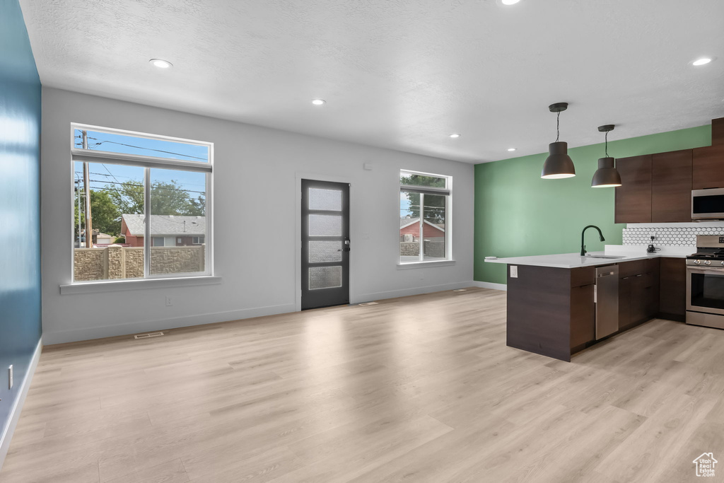 Kitchen with stainless steel appliances, a peninsula, modern cabinets, light countertops, and baseboards