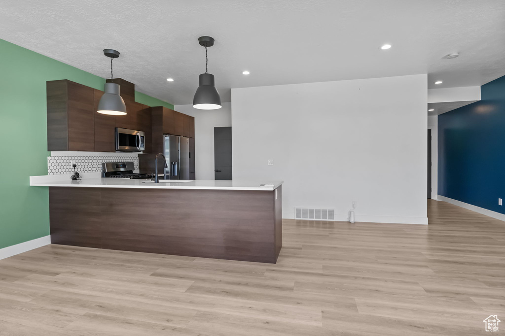 Kitchen featuring appliances with stainless steel finishes, modern cabinets, a peninsula, light countertops, and recessed lighting