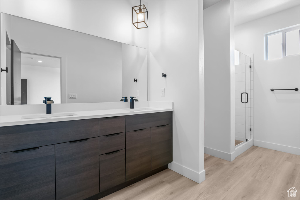 Full bath featuring wood finished floors, double vanity, baseboards, and a stall shower