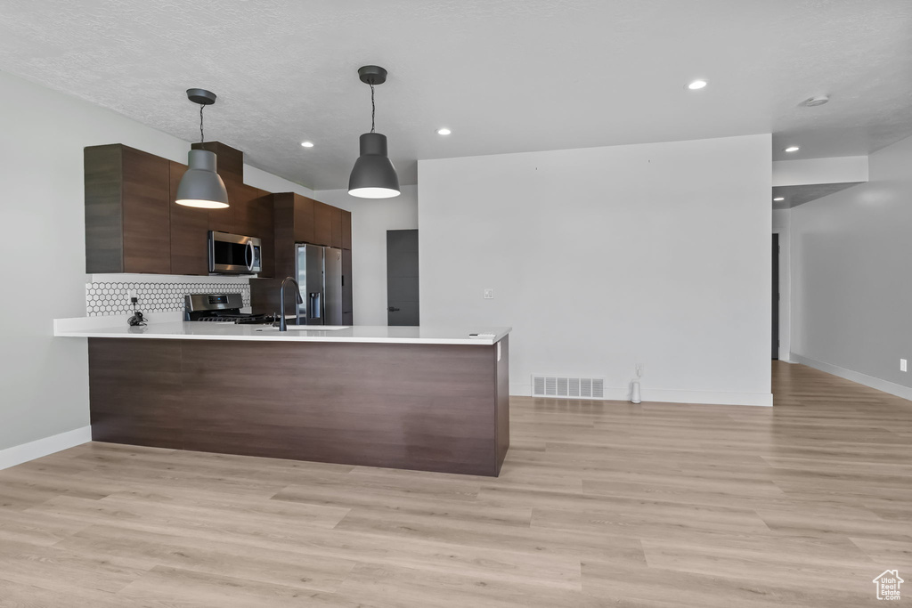 Kitchen with appliances with stainless steel finishes, modern cabinets, a peninsula, light countertops, and recessed lighting