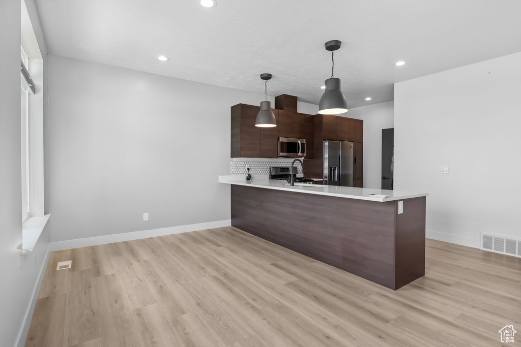 Kitchen featuring appliances with stainless steel finishes, light countertops, a peninsula, modern cabinets, and light wood-type flooring