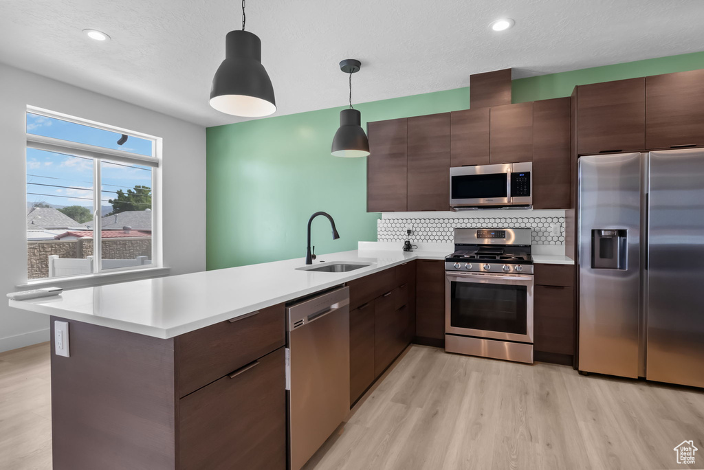 Kitchen featuring appliances with stainless steel finishes, a sink, a peninsula, light wood finished floors, and recessed lighting