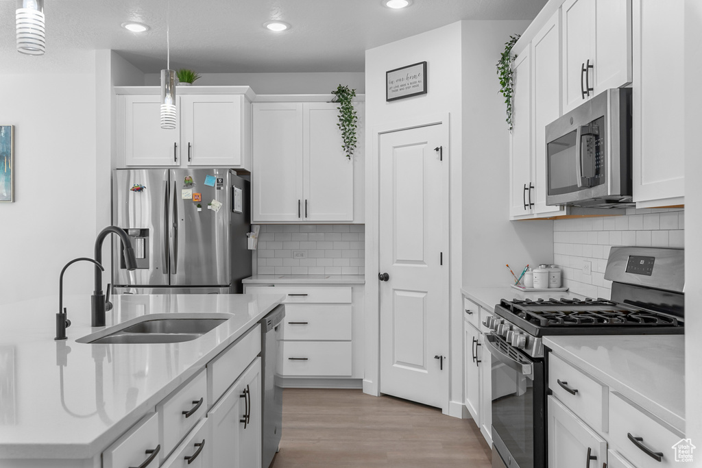Kitchen featuring appliances with stainless steel finishes, recessed lighting, a sink, light wood-style floors, and decorative light fixtures
