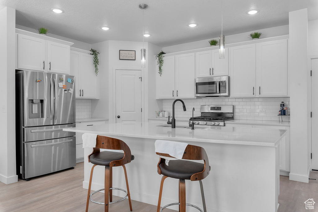 Kitchen featuring appliances with stainless steel finishes, light countertops, light wood-style flooring, recessed lighting, and an island with sink