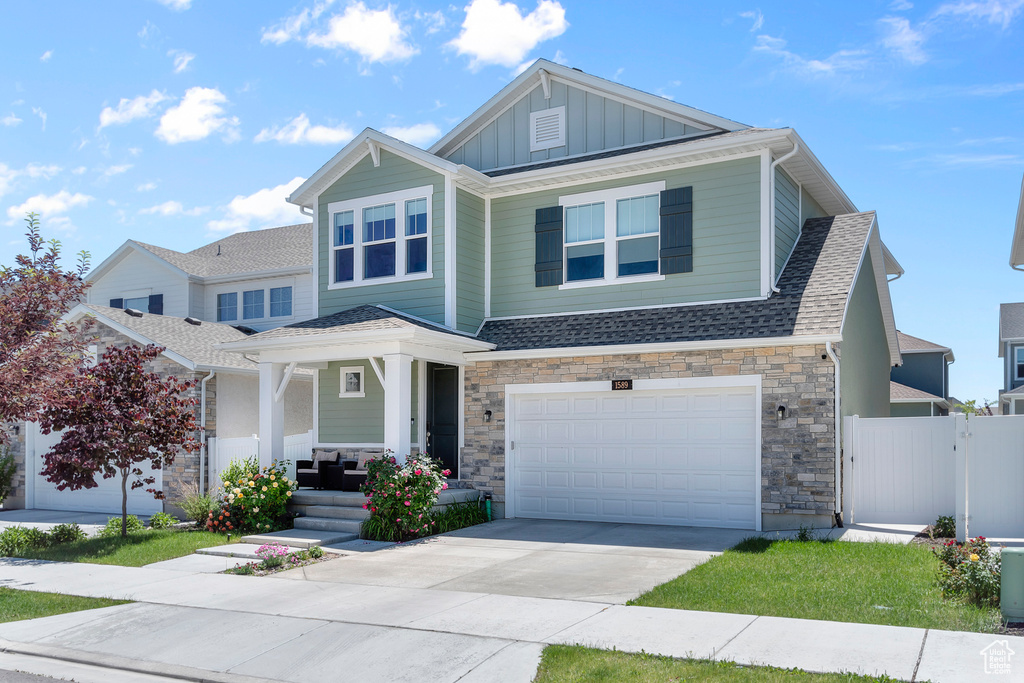 Craftsman inspired home with board and batten siding, covered porch, driveway, stone siding, and a garage