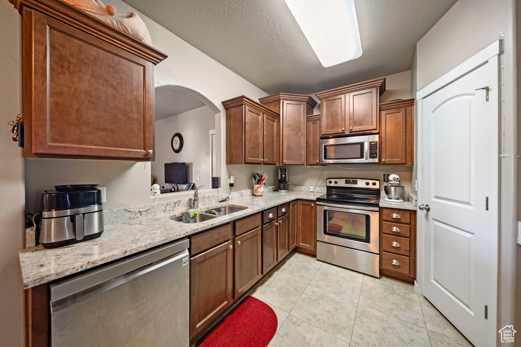 Kitchen featuring stainless steel appliances, a sink, light tile patterned flooring, and light stone countertops