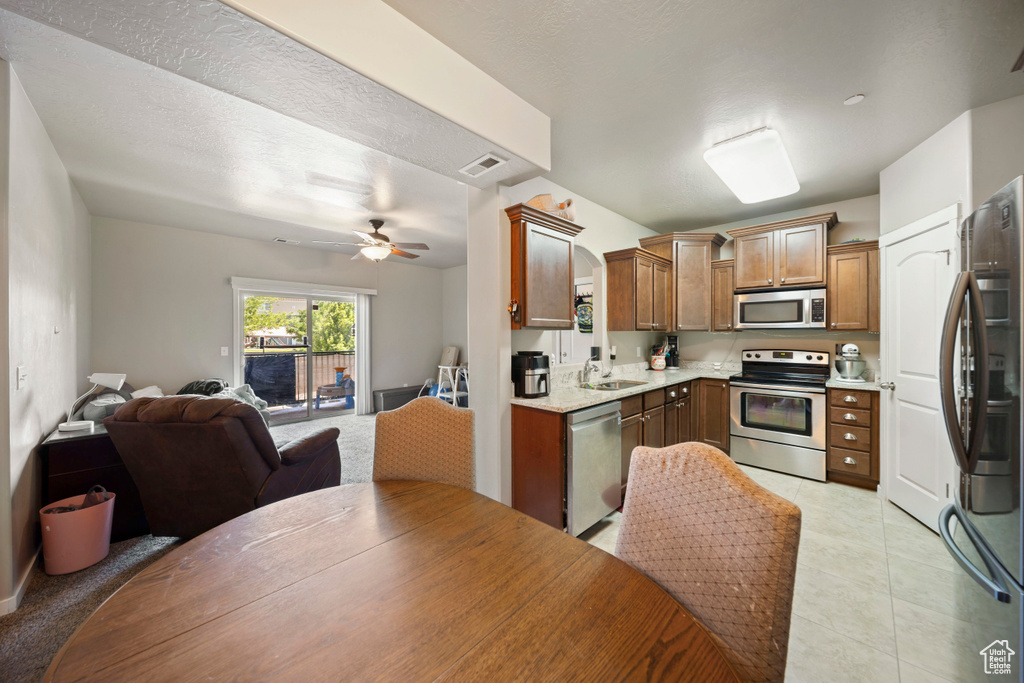 Kitchen with stainless steel appliances, open floor plan, a sink, brown cabinetry, and a ceiling fan