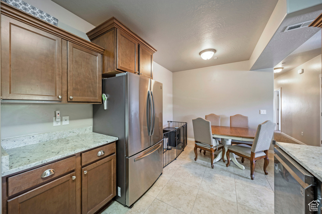 Kitchen featuring freestanding refrigerator, light stone countertops, light tile patterned floors, and baseboards
