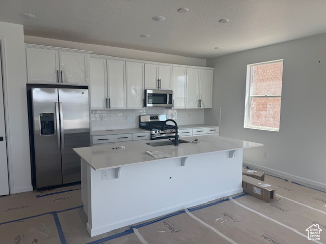 Kitchen with appliances with stainless steel finishes, a sink, tasteful backsplash, a kitchen island with sink, and white cabinets