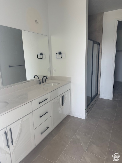 Full bath with double vanity, a stall shower, baseboards, and tile patterned flooring