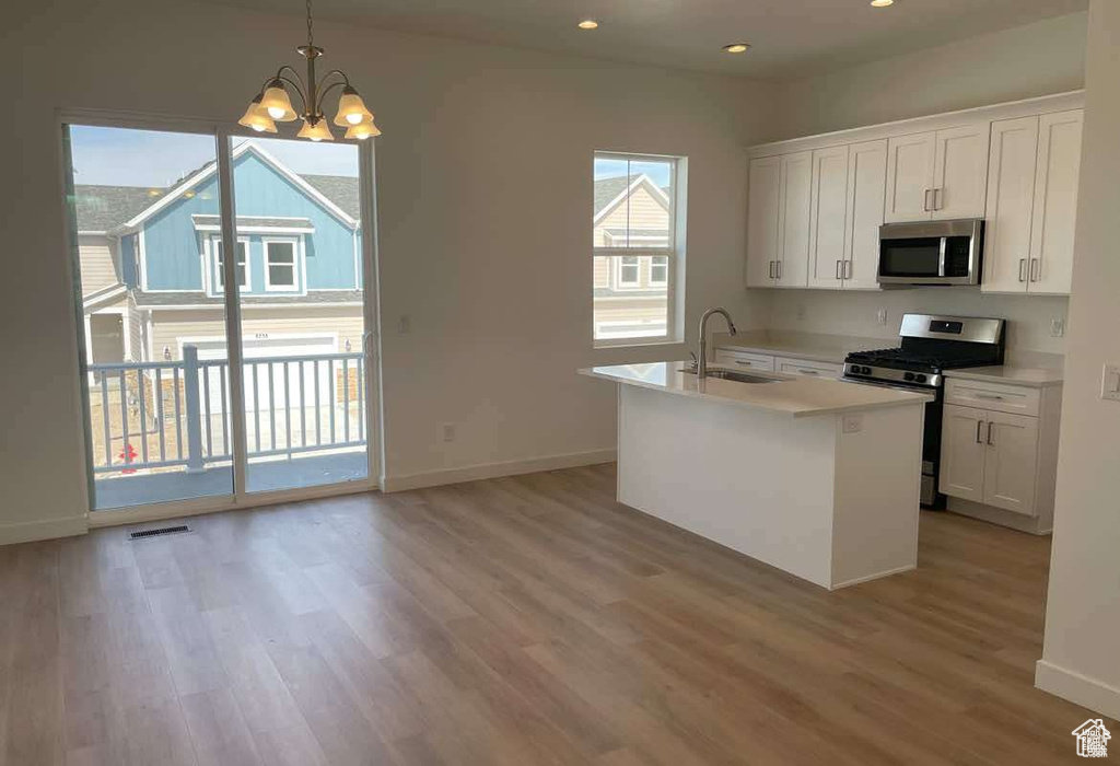 Kitchen with appliances with stainless steel finishes, a sink, light wood finished floors, baseboards, and white cabinets