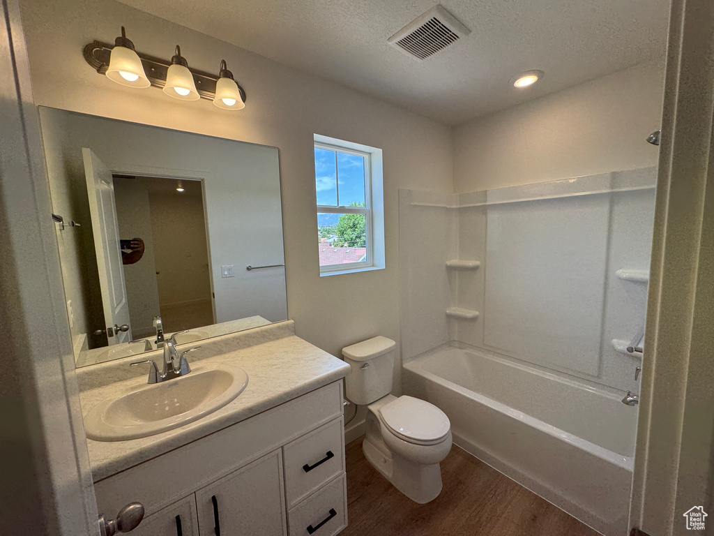Full bath featuring wood finished floors, vanity, a textured ceiling, and  shower combination