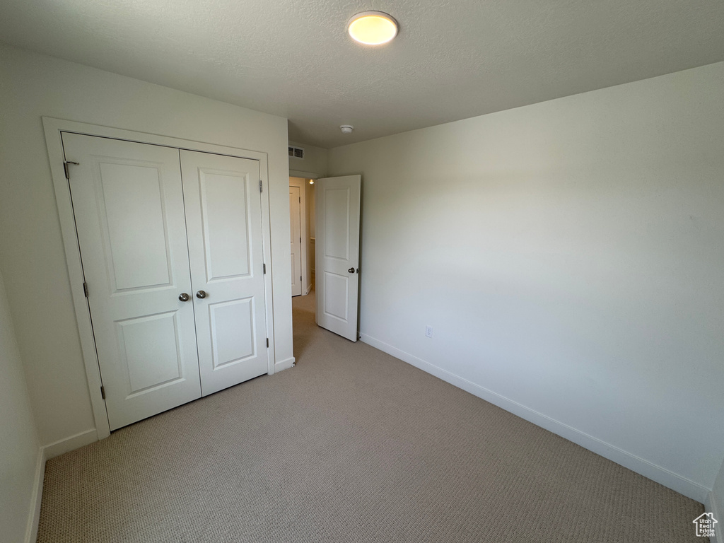 Unfurnished bedroom featuring light carpet and a closet