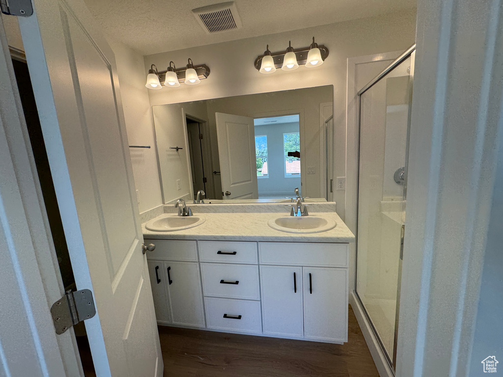 Bathroom featuring a shower stall, double vanity, and wood finished floors