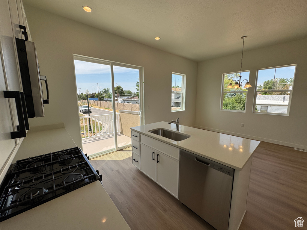 Kitchen featuring dishwasher, wood finished floors, range with gas stovetop, white cabinetry, and light countertops
