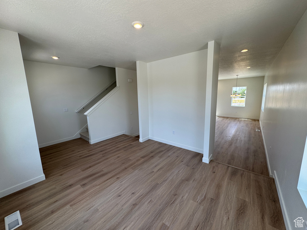 Unfurnished room featuring a chandelier, wood finished floors, recessed lighting, stairway, and a textured ceiling
