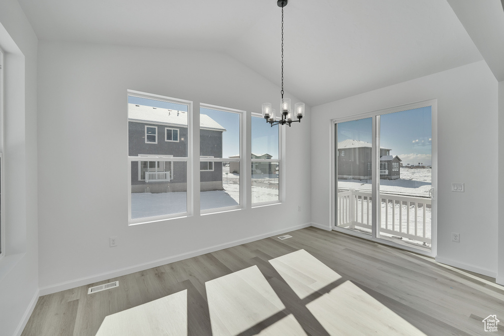 Unfurnished dining area with a chandelier, vaulted ceiling, wood finished floors, and baseboards