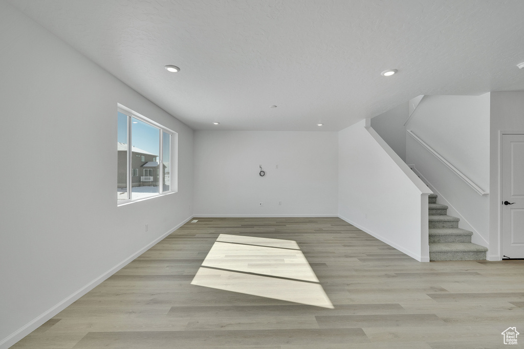 Unfurnished living room with recessed lighting, baseboards, light wood-style floors, and stairway
