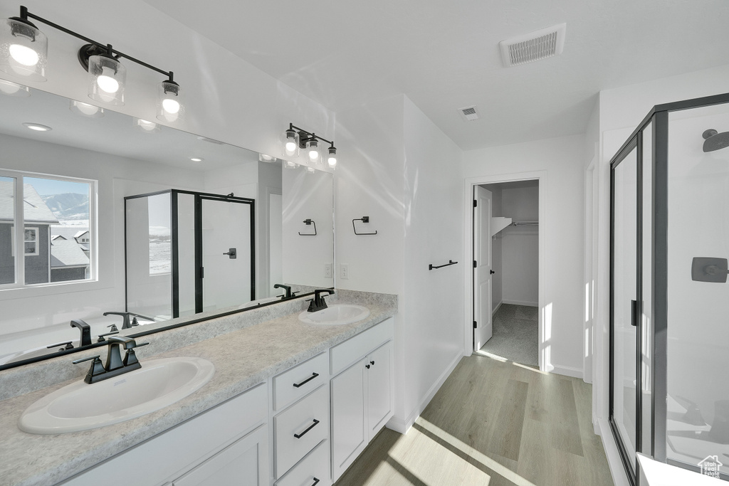 Full bathroom featuring a shower stall, wood finished floors, double vanity, and baseboards