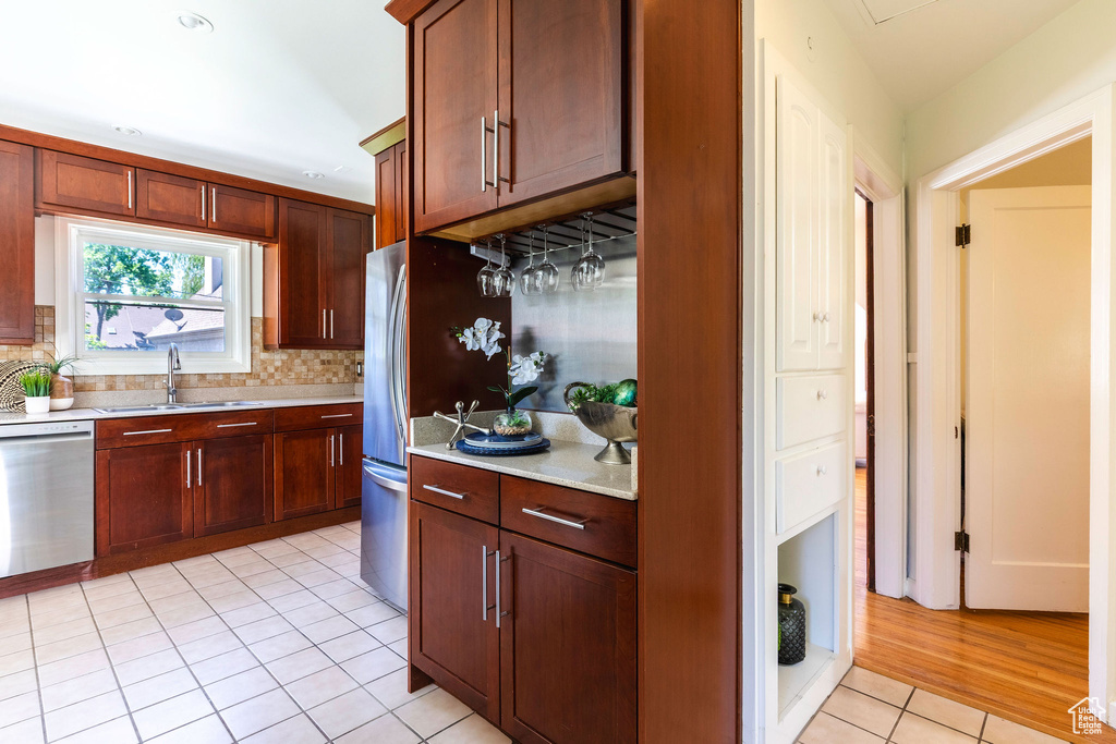 Kitchen featuring appliances with stainless steel finishes, a sink, light tile patterned flooring, and tasteful backsplash