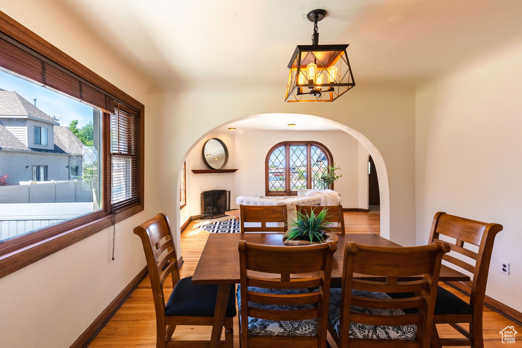 Dining area featuring arched walkways, a chandelier, light wood-style flooring, baseboards, and a fireplace with raised hearth