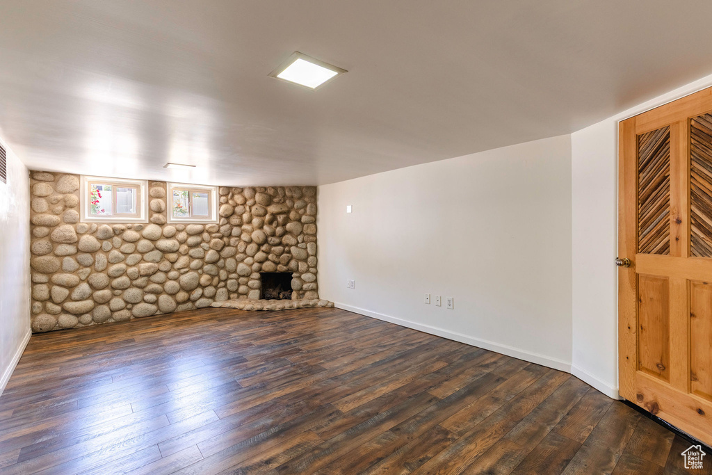 Unfurnished living room with dark wood-style flooring, a stone fireplace, and baseboards