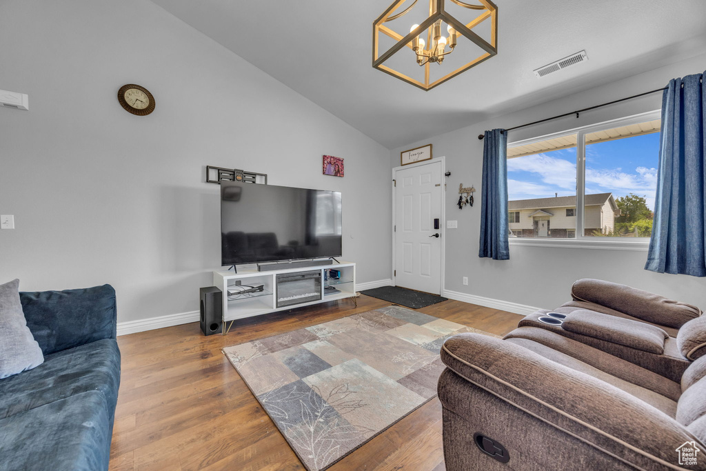 Living room with a chandelier, wood finished floors, lofted ceiling, and baseboards