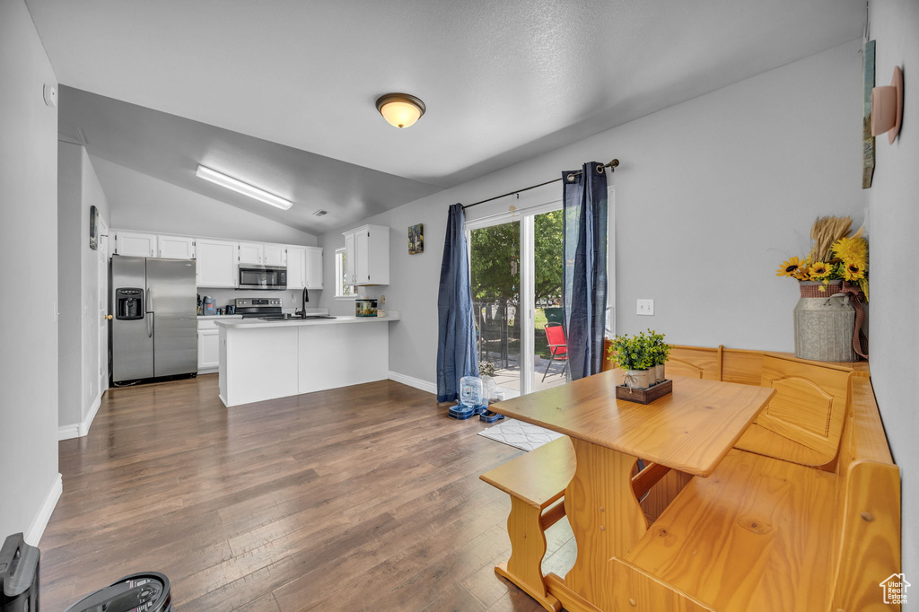 Kitchen featuring appliances with stainless steel finishes, a peninsula, vaulted ceiling, a sink, and dark wood-style floors