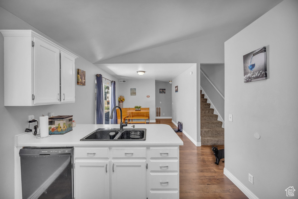 Kitchen featuring dishwashing machine, a sink, a peninsula, white cabinetry, and lofted ceiling