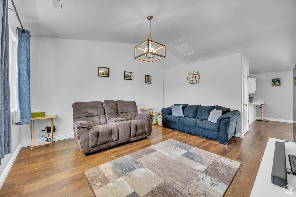 Living room featuring a chandelier, wood finished floors, baseboards, and vaulted ceiling