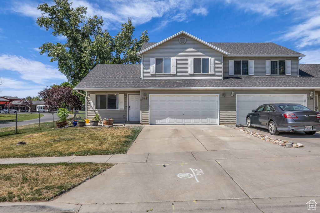 View of front of property featuring concrete driveway, an attached garage, a front lawn, and roof with shingles